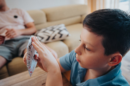 Young boy intensely focused on playing cards game in the living roomの写真素材