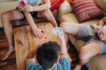 Older teenagers playing card games with their younger brother in living roomの写真素材