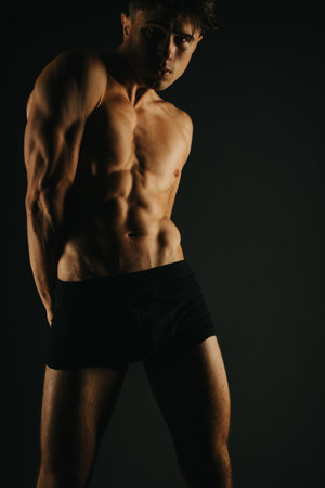 Fit male showcasing his abs and muscular arms in low lightの写真素材