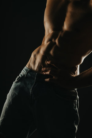 Close-up of a muscular male torso highlighting abs and muscles in dim lightingの写真素材
