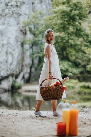Woman enjoying a picnic in nature carrying a basket filled with fresh fruits and breadの写真素材