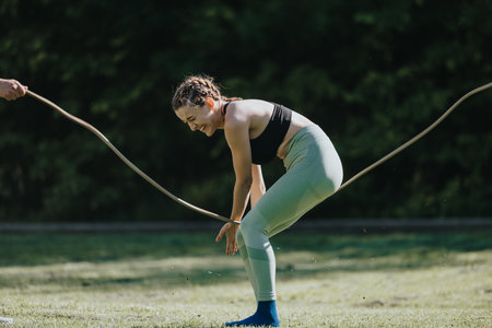 Young woman having fun during fitness exercise with rope outdoors in sunny weather
