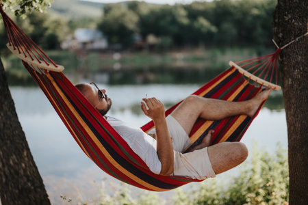 Man relaxing in a hammock by the lake enjoying nature and tranquilityの写真素材