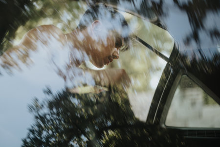 Reflection of a man inside a car through a window with blurred natural foliage