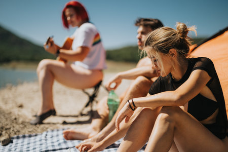 Group of friends enjoying relaxing moments by the lake with guitar music on a summer day
