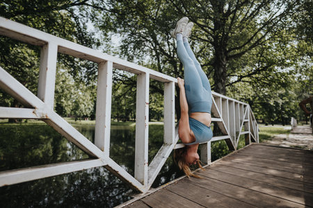 Woman performing handstand on bridge in a park during a sunny dayの写真素材