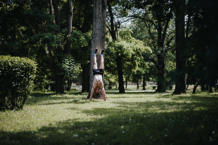 Man doing handstand against tree in a lush green parkの写真素材