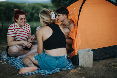Friends enjoying a picnic and playing cards near a tent in natureの写真素材
