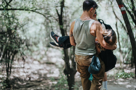 Man carrying woman through a wooded trail during a hike, showcasing outdoor adventure and teamworkの写真素材