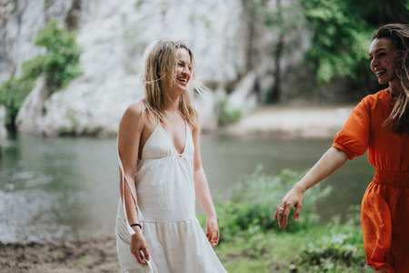 Two women laughing and enjoying nature by a river on a sunny dayの写真素材