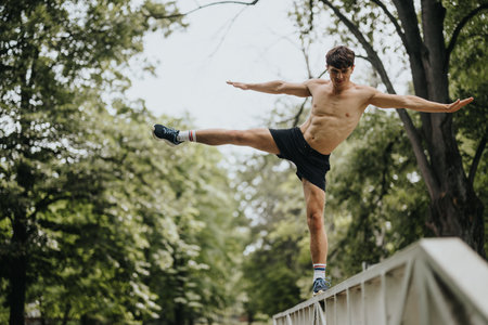 Shirtless man balancing on a bridge railing in a park