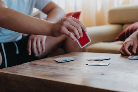 People playing card games sitting at a wooden table in a cozy living roomの写真素材