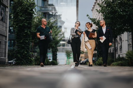 Group of businesspeople walking and discussing documents outdoors in urban setting
