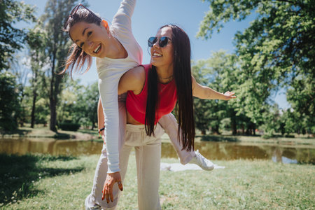 Joyful friends having fun with a piggyback ride in the park on a sunny day