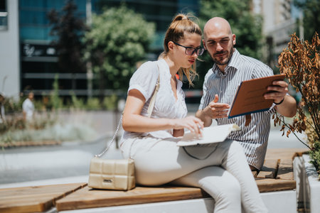 Two people collaborating outside while reviewing documents and digital tablet in an urban settingの写真素材