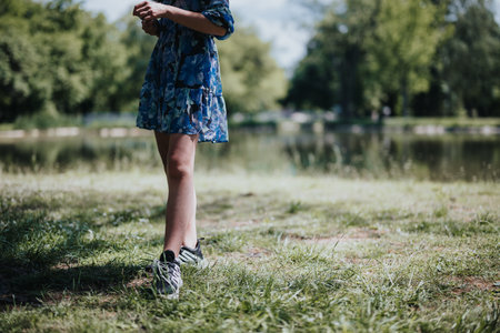 Young woman enjoying a peaceful walk by the lake in a park, wearing a floral dressの写真素材