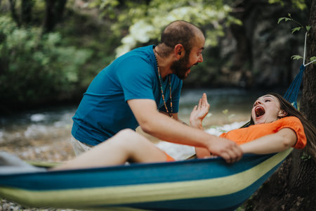 Playful couple laughing and enjoying time together in a hammock by a scenic riverの写真素材