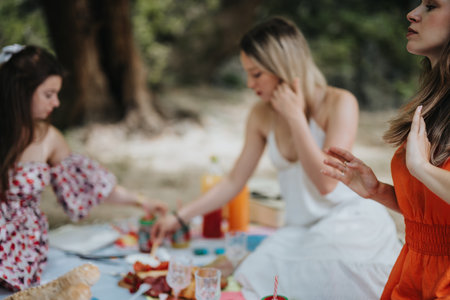 Young women enjoying a picnic in the park with food and drinks on a sunny dayの写真素材