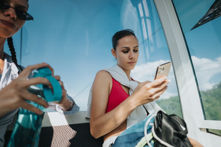 Young women traveling in cable car, using smart phones and hydrating in summerの写真素材