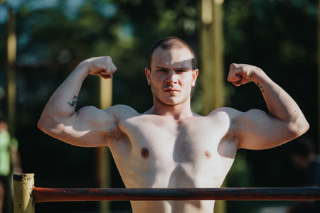 Young man showcasing muscular physique by flexing his biceps outdoors