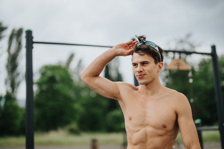 Fit young man adjusting sunglasses at outdoor gym with parallel bars