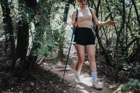 Young woman hiking on a sunny day through a forest trail, enjoying nature and adventureの写真素材