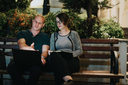 Business colleagues working outdoors at night on wooden bench with laptop and notebookの写真素材