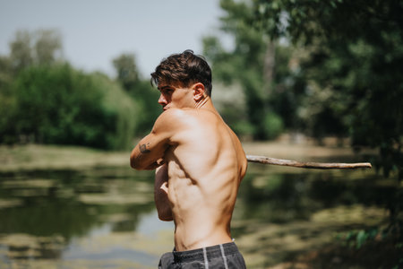 Man exercising with a stick by the lake in a serene natural settingの写真素材
