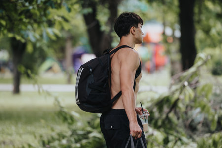 Fit young man with backpack walking in park with smoothie in handの写真素材
