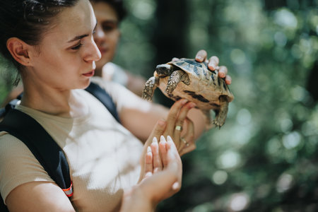 Young woman holding a turtle in the forest during a summer hike with friendsの写真素材