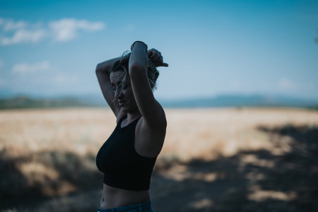 Young woman enjoying a sunny day outdoors in a scenic field, tying her hair upの写真素材