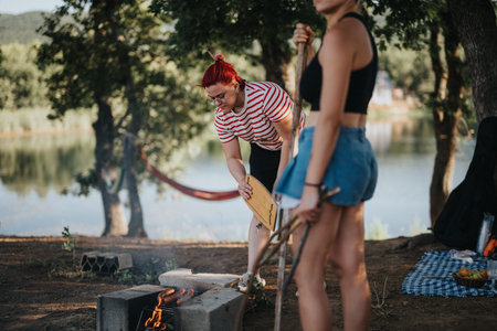Friends enjoying a picnic by the lake with a campfire on a sunny day in natureの写真素材