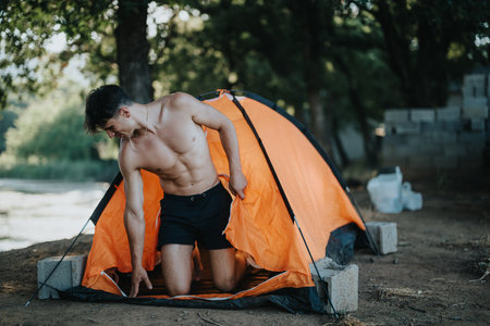 Young man enjoying a summer day camping in nature in an orange tentの写真素材