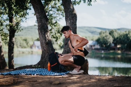 Shirtless man enjoying a summer picnic by the lake in a forest settingの写真素材