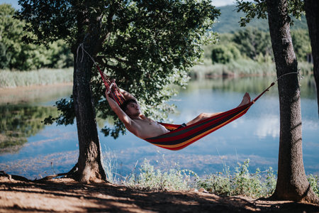 Man relaxing in a hammock by the lake during a summer dayの写真素材