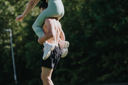Athletic couple performing an acrobatic lift in the park with trees in the backgroundの写真素材