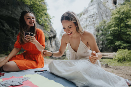 Two women enjoying a picnic in nature, playing cards and laughingの写真素材