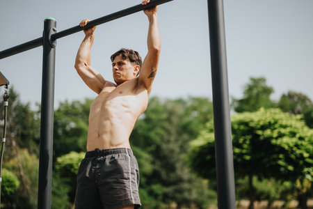 Young man performing pull-ups outdoors in a scenic park setting on a sunny dayの写真素材