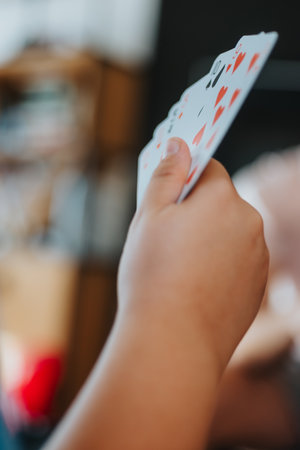 Close-up of a person holding a hand of playing cards during a family game at homeの写真素材