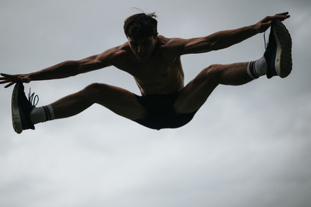 Man practicing high jumps on a cloudy day depicting strength and agilityの写真素材