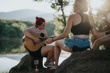 Friends enjoying music in nature by a lake on a sunny dayの写真素材
