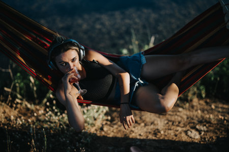 Woman relaxing on hammock with a drink, enjoying summer day in natureの写真素材