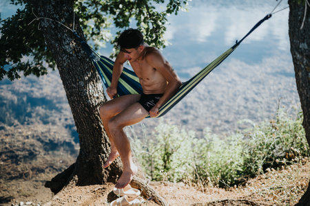 Young man relaxing in a hammock by the lake during a summer adventureの写真素材