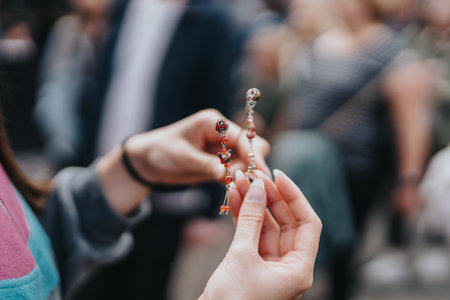 Close-up of hands holding beautiful handcrafted jewelry with delicate details at an outdoor marketの写真素材