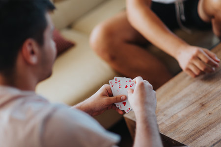 Two young men playing a card game together on a wooden table, enjoying a relaxed day indoorsの写真素材