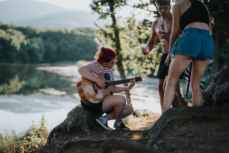 Friends enjoying nature with guitar and wine by a lake on a summer dayの写真素材