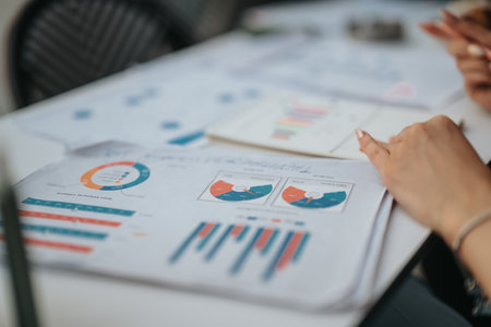 Business meeting with data analysis and charts on documents, hands pointing at the reports on the...