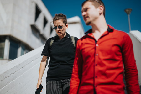 Business professionals walking outside building with focus on woman in black and man in redの写真素材