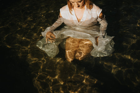 Woman in white dress submerged in water creating a serene and reflective atmosphereの写真素材
