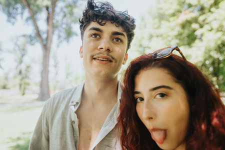 Two young adults enjoying a sunny day at the park with playful expressions
